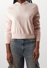 Hellrosa Kapuzenpullover mit geripptem Saum und Bündchen, ausgestattet mit einer Kordelzugkapuze und Raglanärmeln, kombiniert mit hellblauen Denim-Jeans.
