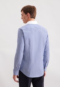 Camicia a righe blu e bianca con colletto a punta, maniche lunghe e dettaglio a bottoni sui polsini; tessuto liscio con vestibilità su misura.