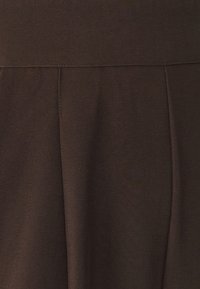 Smeđa suknja od mekog, teksturiranog tkanja. Ima glatki pojas i nabore za lepršav siluetu. Jednostavan, čist šav.