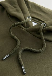 Oliven grøn hoodie har en snøre med vævet tekstur og metalender, sat mod en glat stofbaggrund.
