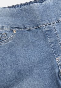 Denimtyg i ljusblått med en jämn textur. Har en standard midja, knappstängning och kontrasterande stygn längs sömmarna.