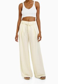 Vit ribbad cropped tanktopp i kombination med ljusgula vida byxor med dragsko i midjan och veck, bärs med plattformssandaletter.