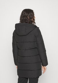 Abrigo acolchado negro con capucha, presenta un diseño acolchado, mangas largas y detalles de canalé en secciones. Tejido suave y ligero.