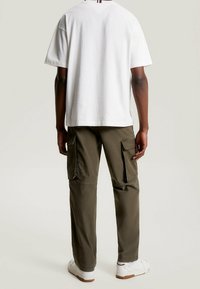 Camiseta blanca de algodón de manga corta, combinada con pantalones cargo verdes oliva con grandes bolsillos laterales, llevados con zapatillas blancas.