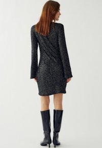 Rochie mini neagră cu paiete, cu mâneci lungi și o siluetă fitted. Asortată cu cizme negre cu toc înalt până la genunchi, evidențiind un design elegant.