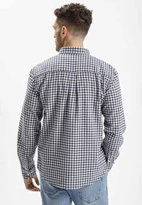 Koszula z długim rękawem w czarno-białą kratę. Kołnierzyk zapinany na guziki, detal na plecach i dopasowane mankiety. Materiał bawełniany.