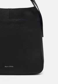 Bolso hobo de piel negra con un acabado texturizado, que presenta un sutil logotipo en la parte inferior y una única correa para el hombro.