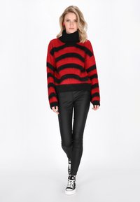 Pulover în dungi roșii și negre, cu un guler înalt, confecționat dintr-un material pufoșel, asortat cu pantaloni din piele negri și adidași negri.