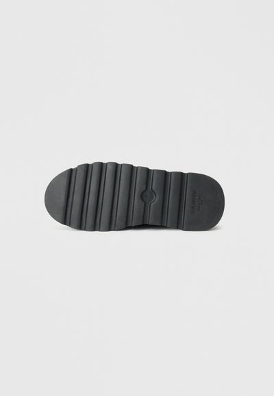 Sola de sapato de borracha preta com ranhuras horizontais, bico arredondado e detalhe do logo em relevo. Textura lisa com um design sólido e plano.