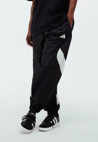 Black athletic pants with white side panels, elastic cuffs, and a discreet logo on the thigh. Fabric appears smooth and lightweight.