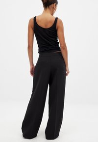 Juodi plačios kojų kelnės su galinėmis kišenėmis, lygiu paviršiumi ir švariomis linijomis. Derinamos su prigludusia juoda marškinėliais be rankovių.