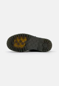 Black rubber shoe sole featuring a multi-directional tread pattern with yellow accents and textured surface for improved grip and durability.