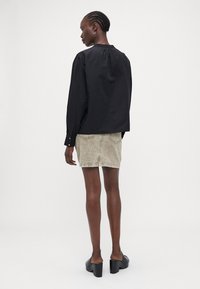 Black long-sleeve blouse with a round neckline and gathered back, paired with a light beige denim skirt and black chunky heeled mules.