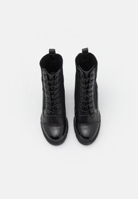 Black ankle boots featuring a smooth leather toe cap, textile sides, and laces. Ribbed fabric collar, flat rubber sole, and decorative stitching.