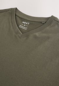 Olijfgroene V-hals T-shirt met de tekst "NEXT M Regular Fit Made in Bangladesh" gedrukt aan de binnenkant van de kraag.