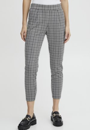 Pantalones grises ajustados hasta el tobillo con patrón de cuadros negros, combinados con mocasines negros y una blusa blanca.