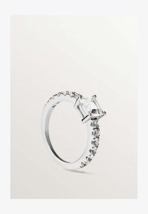 Anillo de plata con una piedra preciosa central transparente de corte esmeralda y piedras redondas más pequeñas a lo largo de la banda sobre un fondo claro.