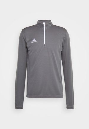 Sivý športový top s dlhým rukávom a štvrť zipom, s bielym zipsom a vyšitou logom Adidas na ľavom prsníku. Hladká textúra.
