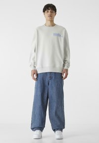 Világosszürke pulóver kék felirattal, laza kék farmernadrággal és fehér sportcipővel párosítva. Egyszerű dizájn és laza viselet.