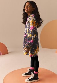 Felpa con cappuccio tie-dye in viola, giallo e rosa. Abbinata a leggings neri e sneakers alte nere con dettagli rosa.