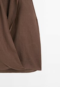 Jupe en lin marron avec un devant style portefeuille et des plis subtils suspendue sur un fond blanc.