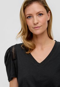 Zwarte V-hals T-shirt met pofmouwen, met kantdetails op de schouder. Glad stof met een ontspannen pasvorm.