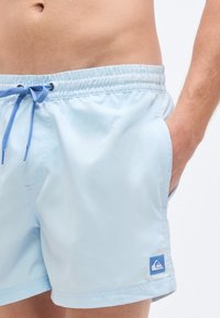 Σορτς κολύμβησης σε ανοιχτό μπλε χρώμα, κατασκευασμένα από απαλό, γρήγορα στεγνωτικό ύφασμα. Διαθέτουν ελαστική μέση με ρυθμιζόμενο κορδόνι και πλαϊνές τσέπες.