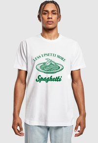 T-shirt en coton blanc avec un design graphique de spaghetti dans une assiette et un texte en vert qui dit "MOINS D'UPSETTI, PLUS DE SPAGHETTI."