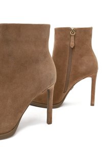 Bottines en daim marron avec un design affiné, des talons aiguilles hauts et un détail de fermeture éclair sur le côté. Texture lisse et style minimaliste.