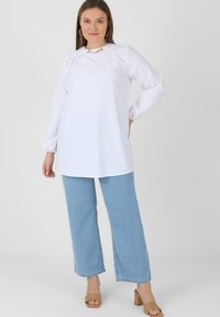 White long-sleeve top with gathered details at the shoulders, paired with light blue wide-leg jeans and beige block-heeled sandals.