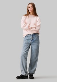 Maglione oversize rosa chiaro in lana con scollo a coste, abbinato a jeans blu a vita alta e larghi e scarpe con tacco nero.