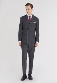 Szary w kratę podwójnie zapinany garnitur o dopasowanym kroju, biała koszula i czerwona krawat w kropki. W skład zestawu wchodzi czerwona i biała kraciasta poszetka. Czarne buty.