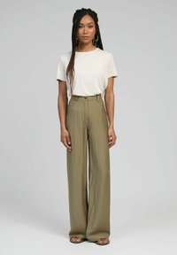 T-shirt beige associé à un pantalon large taille haute en kaki. Le pantalon présente une fermeture à bouton et des passants de ceinture, avec une texture lisse et légère.