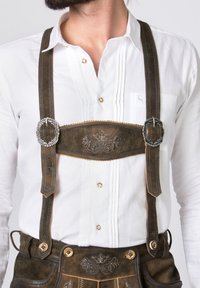 Braune Lederhosen mit dekorativer Stickerei, weißes Hemd mit Falten und silberne Schnallen an den Hosenträgern.