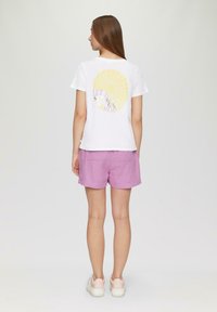 Wit T-shirt met korte mouwen, voorzien van een gele zonafbeelding en tekst op de achterkant. Gekocht met roze shorts en witte platform sneakers.