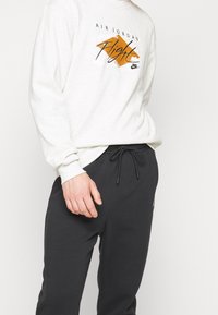 Ljusgrå sweatshirt med "Air Jordan Flight" grafik i orange och svart, ihop med mörkgrå sportbyxor med dragsko midja.