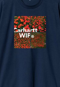 Granatowa koszulka z okrągłym nadrukiem składającym się z czterech części z żywymi czerwonymi kwiatami. Logo "Carhartt WIP" w białym kolorze umieszczone na dole na środku.