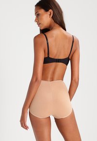 Black bra with adjustable straps, paired with tan high-waisted shorts. Smooth texture, seamless design, and minimal stitching detail.