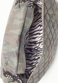 Bolso de camuflaje acolchado con una correa de cadena plateada, que presenta un interior a rayas en blanco y negro y un bolsillo con cremallera.