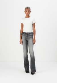 Jeans grigi flared con un finish sbiadito, abbinati a una camicia aderente bianca a maniche corte. Cintura nera con una fibbia circolare dorata.