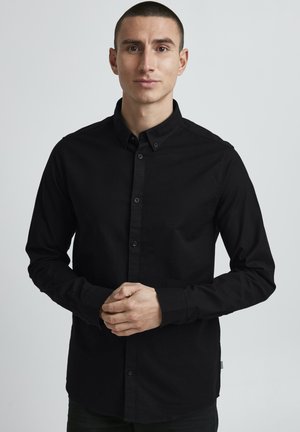 Black button-up shirt made of soft cotton with long sleeves, a pointed collar, and a fitted design. Features front buttons and a side tag.