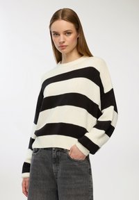 Czarny i biały sweter w paski o luźnym kroju z okrągłym dekoltem i ściągaczami na rękawach, w zestawie z szarymi jeansami o wysokim stanie.