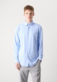 Camisa de botones azul claro hecha de tela suave, con mangas largas y cuello puntiagudo, combinada con pantalones gris. Diseño simple y ajustado.