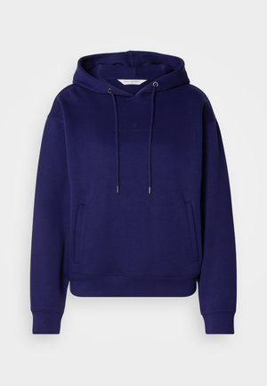 Tumši zils kapuci krekls ar izsistu tekstūru, priekšējo kabatu tipa "kangaroo" un metāla saites stiprinājumiem. Diskreta logo detaļa uz krūtīm.