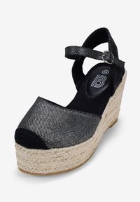 Espadrille noire à compensé avec une tige en textile, une bride cheville et une semelle en jute tressé. Présente un bout arrondi et un détail de surface texturé.