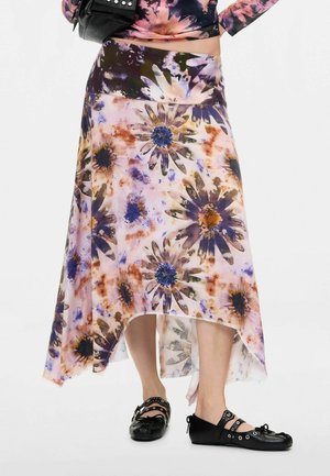 Persona che indossa una gonna floreale asimmetrica nei toni del viola, blu e marrone, ballerine nere borchiate e porta una borsa nera.