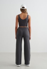 Szary zestaw odzieży sportowej składający się z dopasowanego krótkiego topu z niskim dekoltem na plecach oraz spodni z szerokimi nogawkami i rozcięciami po bokach, uzupełniony białą czapką i sneakersami.