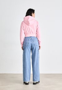 Rosa cropped hettegenser med snorhette og ribbestrikket kant, kombinert med lyseblå vide cargo-jeans med sidelommer.