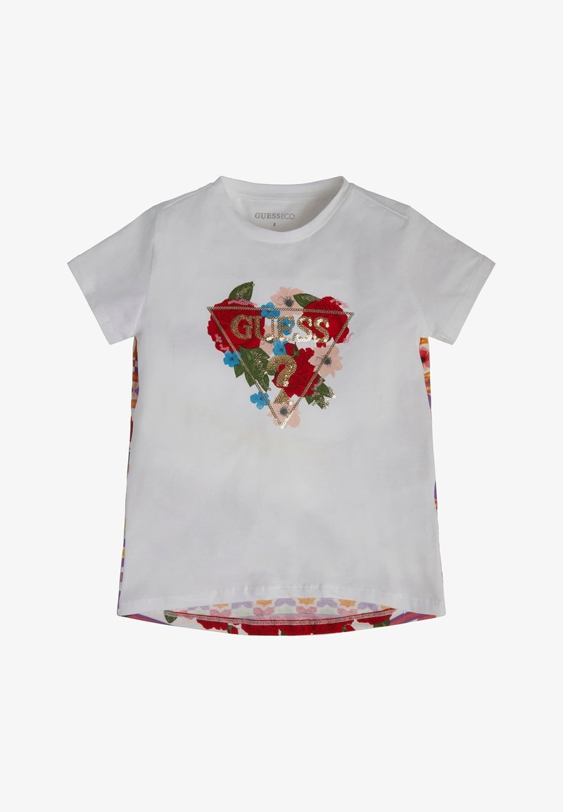 T-shirt blanc à manches courtes avec un motif floral et le logo "GUESS ?" en sequins dorés à l’intérieur d’un triangle sur le devant.