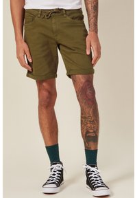 Pantaloni corti verde oliva con risvolti, vita regolabile con cordino e due tasche frontali. Abbinati a sneakers alte nere e calze verdi.